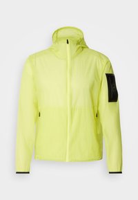 Coupe-vent vert clair à capuche avec fermeture éclair frontale, poches latérales zippées et écusson noir sur la manche gauche.