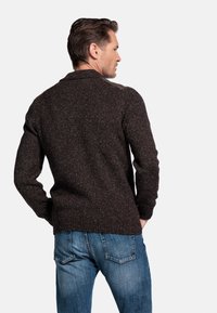 Donkerbruin gebreid sweater met een gestructureerde afwerking, met een kraaghalslijn en geribde manchetten, gecombineerd met blauwe denim jeans.