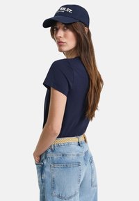 Navy t-shirt with short sleeves paired with light blue denim jeans and a navy baseball cap featuring white text. Textured beige belt visible.