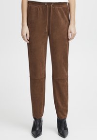 Brown suede jogger pants with an elastic waistband and drawstring. Slim fit, tapered legs with a smooth texture, paired with black ankle boots.