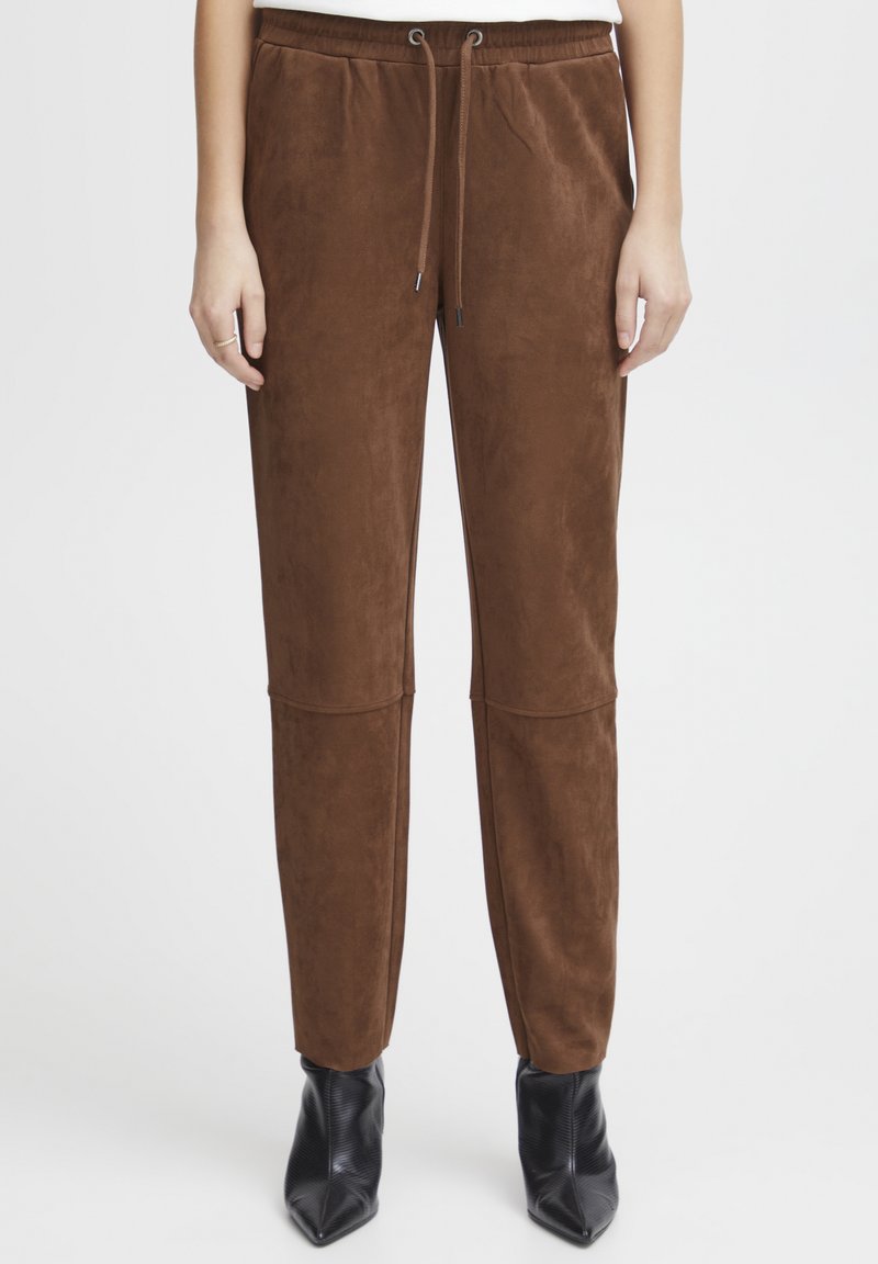 Brown suede jogger pants with an elastic waistband and drawstring. Slim fit, tapered legs with a smooth texture, paired with black ankle boots.
