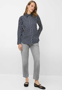 Camicia a righe blu navy e bianca con bottoni e maniche lunghe, abbinata a jeans grigio chiaro a gamba dritta e scarpe basse nere in mesh.