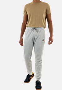 Tan short-sleeve t-shirt paired with gray sweatpants featuring an elastic waistband and drawstring, worn with black sneakers with orange accents.