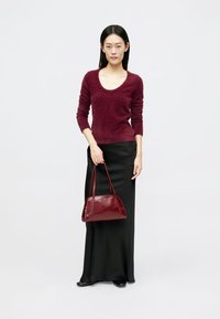 Pulover fuzzy burgundy, fustă maxi din satin negru și o geantă structurată asortată cu un model capitonat și mânere scurte.