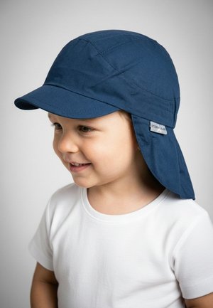 Toddler wearing a navy blue sun hat with neck flap and white t-shirt, smiling and looking to the side against a plain gray background.