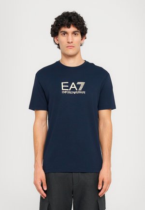 Navy blue t-shirt made of cotton with a round neckline. Features a contrasting light-colored logo "EA7 EMPORIO ARMANI" printed on the front.