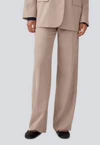 Beige wide-leg trousers made from a smooth fabric with front creases, side pockets, and a relaxed fit. Worn with black flat shoes.