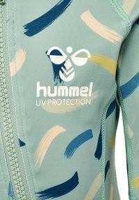 Lättvikts UV-skyddande rashguard i teal för barn med abstrakta penseldragmönster i marinblått, kräm och gult, med dragkedja fram.