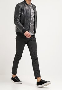 Zwarte leren bomberjack met geribbelde manchetten, grijs tie-dye t-shirt, zwarte slim-fit broek en zwarte sneakers met witte zolen.