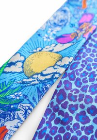 Kleurrijke stof met een heldere blauwe achtergrond. Heeft aan de ene zijde patronen van zon, wolken en tropische flora; aan de andere zijde paarse luipaardprint.