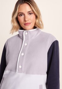 Fleece pullover in light purple and navy, featuring a high collar, white trim, and button closures, with a soft texture and color-block design.