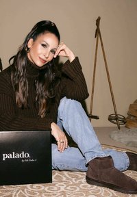 Bruine wollen turtleneck trui, lichtblauwe jeans en donkerbruine leren enkellaarsjes. Zwarte doos gelabeld "palado" ernaast. Getextureerd tapijt eronder.