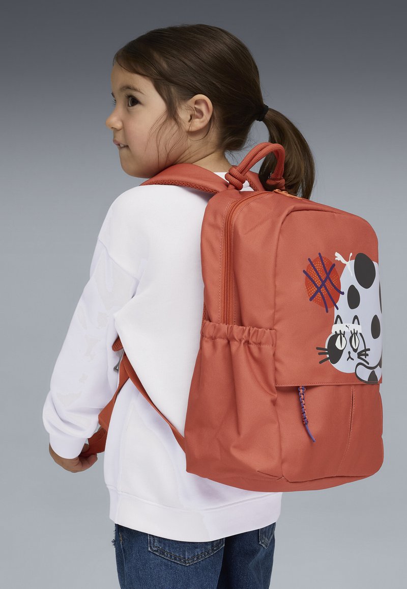 Sac à dos en tissu orange avec un motif ludique de chat sur le devant, équipé d'une poche zippée et de bretelles ajustables.