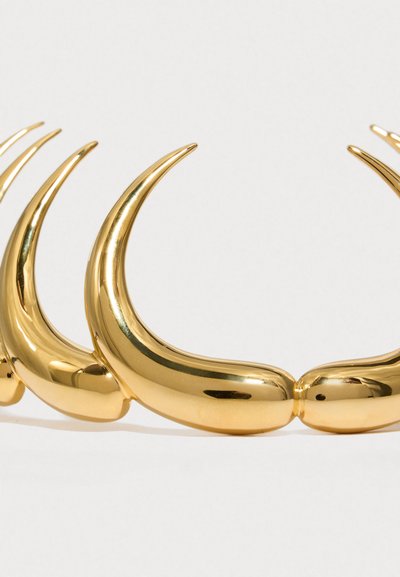 Χρυσό μεταλλικό αξεσουάρ μαλλιών με καμπυλωτά, κέρατο-όμοια σχήματα και λεία, ανακλαστική επιφάνεια. Ο σχεδιασμός αποτελείται από πολλά συνδεδεμένα στοιχεία.