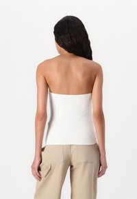Hvit stroppeløs topp med en tettsittende design, jevn tekstur og rett kant, kombinert med beige vide bukser med sidelommer.