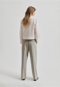 Chaqueta blanca texturizada con un diseño corto, combinada con pantalones de color gris claro. Ambas prendas presentan líneas minimalistas y un corte relajado.