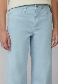 Hellblaue weite Jeans aus weichem Baumwollmaterial, mit Knopfverschluss, fünf Taschen und sichtbaren Nähdetails entlang der Nähte.