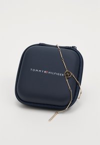Navy blue Tommy Hilfiger zippered case with gold-tone chain featuring a circular logo and a crystal-embellished pendant.