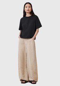 Black relaxed-fit t-shirt with short sleeves, paired with wide-leg beige trousers, featuring a soft texture and subtle side pockets.