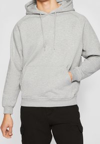Sudadera con capucha gris hecha de tela suave con un bolsillo canguro y cordones ajustables. Cuenta con puños y dobladillo acanalados.