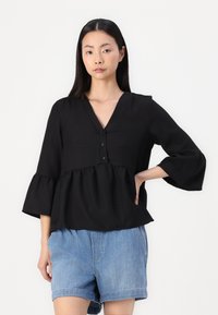 Black peplum top with a V-neck, three buttons at the front, and flared sleeves. Fabric has a textured finish. Paired with denim shorts.