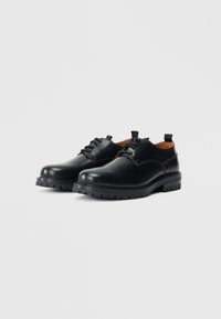 Schwarze Lederschuhe mit einer glatten Oberfläche, runder Zehenpartie und Gummisohle mit sichtbar ausgeprägtem Profil. Enthält Schnürsenkel und Anhänger an der Ferse.