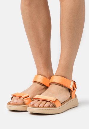 Orange sandals with wide fabric straps, padded footbed, and a beige rubber sole. The design features an adjustable ankle strap.