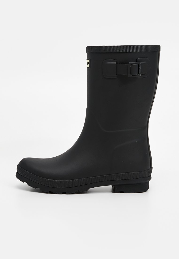 Schwarze Gummiregenstiefel mit glatter Oberfläche, knöchelhoch, kreisförmiger Profilsohle und verstellbarem Schnallendetail an der Seite.