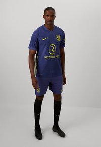 Paarse voetbalshirt met verticale ribbeltextuur, gele accenten en logo; gecombineerd met bijpassende shorts en zwarte sokken.