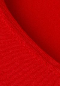 Gros plan sur un tissu rouge tricoté avec une couture détaillée et un bord côtelé, montrant la texture et le motif du tissage.
