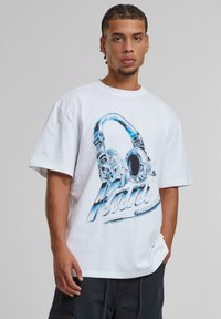 White cotton t-shirt with a blue graphic of headphones and the text "Kani." Short sleeves and a relaxed fit.