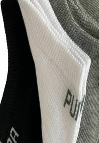 Drei Paar Socken in Schwarz, Weiß und Grau. Jede Socke hat eine gerippte Textur und ein kleines Markenlogo auf dem Stoff.