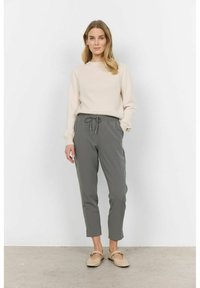 Maglione a coste di un beige chiaro con maniche lunghe abbinato a pantaloni grigi a sigaretta con vita elasticizzata e cordoncino. Scarpe piatte beige.