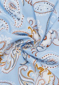 Tessuto azzurro chiaro con motivi paisley in bianco, marrone e blu scuro. La texture appare liscia con dettagli e curve intricate visibili.