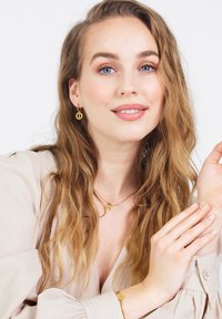 Gouden juwelen set met een paar oorringen, een ketting met een hanger en een armband, gecombineerd met een licht beige blouse. Soepele textuur.