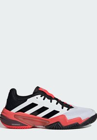 Weiße und schwarze Sportschuhe mit roten Akzenten, Obermaterial aus Mesh, strukturierten Gummisohle und auffälligen schwarzen Streifen an den Seiten.