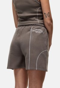 Shorts en coton marron avec des détails de couture blanche, dotés d'une taille à cordon de serrage et de poches latérales. Logo brodé sur la poche arrière.