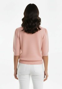 Jasnoróżowy sweter na drutach z krótkimi bufkami i ściągaczami przy rękawach. Stylizowany z białymi dopasowanymi spodniami z teksturowanym wzorem.