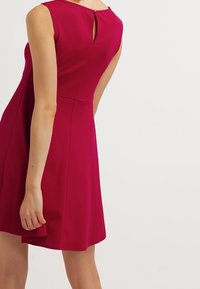Fuchsia ärmelloses Kleid mit tailliertem Oberteil, ausgestelltem Rock und einem Schlüssel-ausschnitt auf der Rückseite. Hergestellt aus einem glatten, dehnbaren Stoff.