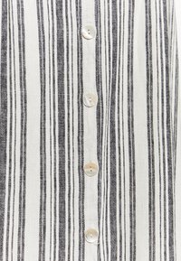 Tissu à rayures noires et blanches avec un devant boutonné, comportant six boutons ronds de couleur claire et une texture légère et douce.