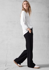 Top blanco de manga larga y pantalones de pierna ancha negros. El conjunto se complementa con zapatillas blancas con suelas beige. Tejido suave, corte relajado.