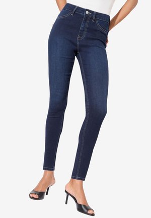 Tumedat sinised kitsad teksad mustade avatud tallaga kõrgete kontsadega muleside ja valge toppiga, näidatud vööst jalatallani.