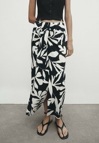 Zwart-wit bloemenprint rok met een wikkelontwerp, gemaakt van lichtgewicht stof, met een zijsplit en gecombineerd met zwarte sandalen.