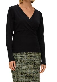 Czarny sweter z długim rękawem, z dekoltem w kształcie litery V i fasonem kopertowym. Na dole znajduje się dopasowana spódnica w wzory z zielonymi kwiatowymi akcentami na czarnym tle.