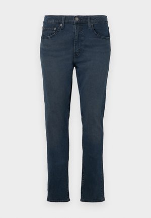 Dark blue denim jeans with a slim fit, standard pockets, and a zip fly. Features visible stitching and a slight fade for texture.