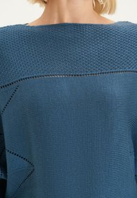 Blauwe gebreide trui met een textuurpatroon, voorzien van een brede halslijn en subtiele open gebreide details langs de naden.