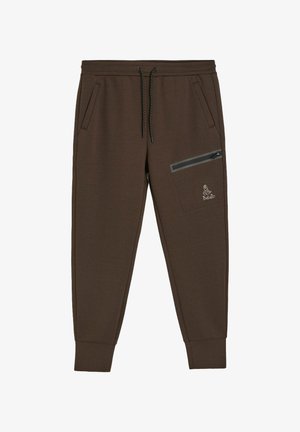 Brązowe dresy wykonane z miękkiego materiału, wyposażone w boczne kieszenie, kieszeń na udzie na zamek oraz elastyczne ściągacze przy kostkach.