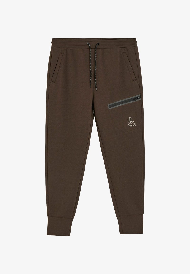 Brązowe dresy wykonane z miękkiego materiału, wyposażone w boczne kieszenie, kieszeń na udzie na zamek oraz elastyczne ściągacze przy kostkach.