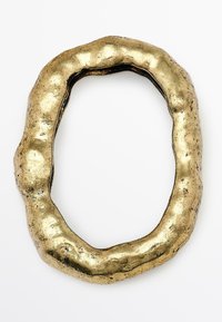 Gouden metalen ring met een onregelmatige, gestructureerde oppervlakte en een ovale vorm, voorzien van een golvend profiel en oneven randen.