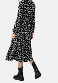 Robe noire à manches longues avec motif floral blanc, longueur fluide, associée à des bottines noires à cheville avec une semelle épaisse.